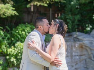 A romantic couple shares intimate kisses in a scenic outdoor setting with lush greenery and stone walls.