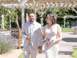 A happy couple walks together under a white pergola decorated with greenery on their wedding day.