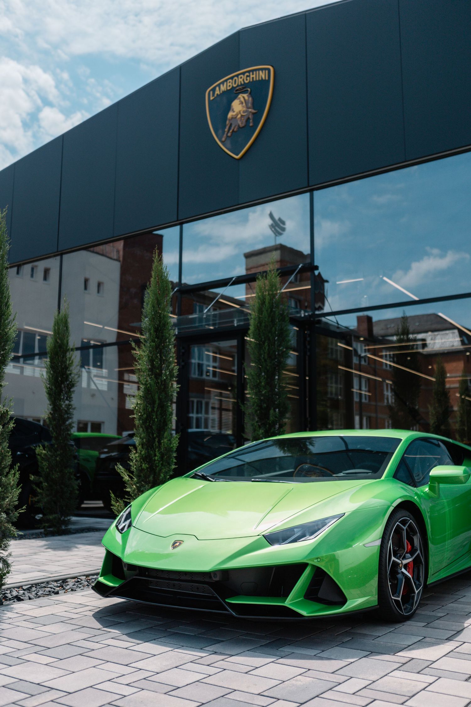 Bright green Lamborghini Huracan EVO parked in front of a modern building with the Lamborghini logo displayed above.