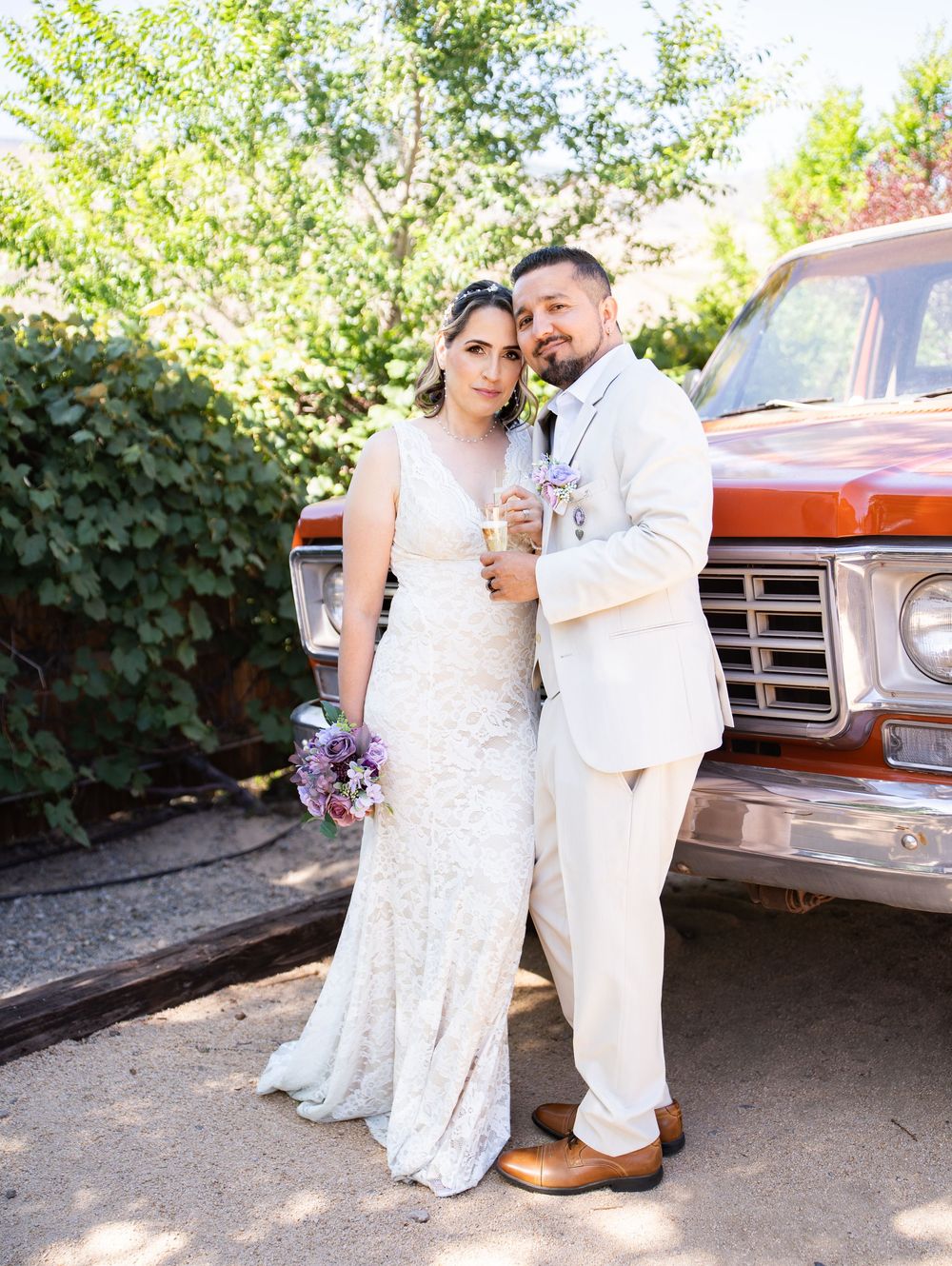 A couple poses in wedding attire in front of a vintage red truck during an outdoor celebration.