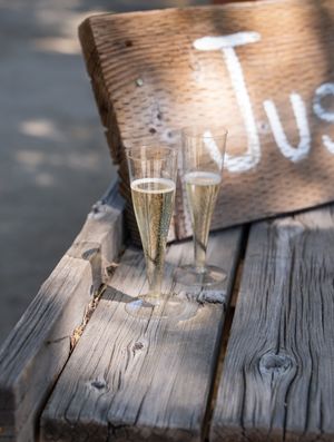 Two champagne flutes filled with bubbly rest on rustic wooden bench with text decoration.