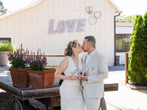 A romantic wedding couple poses together outdoors in front of a white building with decorative planters.