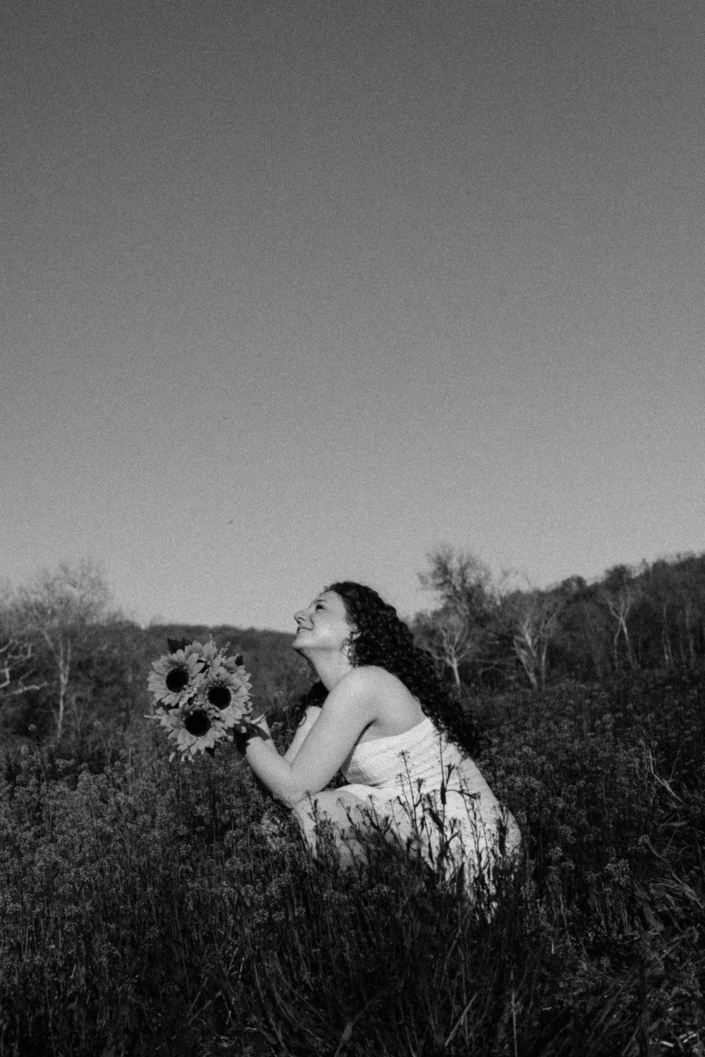 A black and white portrait with sunflowers in a rustic outdoor setting.