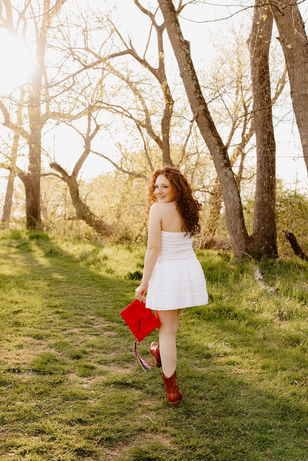 A person in a white dress and red boots walks along a sunlit woodland path.