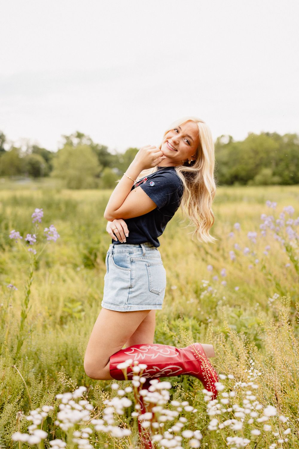 Woman in casual outfit poses playfully in summer wildflower field.