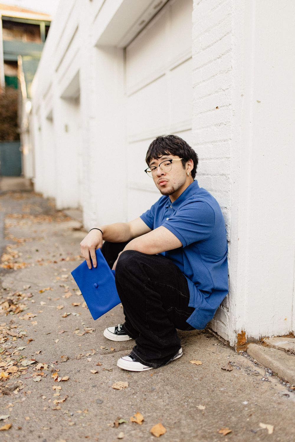 Person wearing blue shirt and glasses sits against white wall with autumn leaves in Frederick Maryland