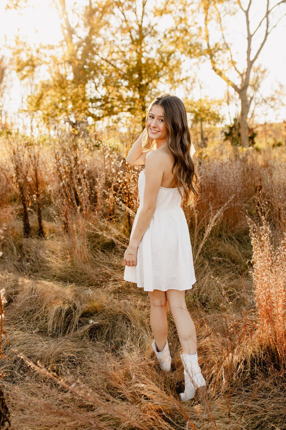 Child in white dress walks through golden field at sunset with dreamy lighting in Frederick Maryland