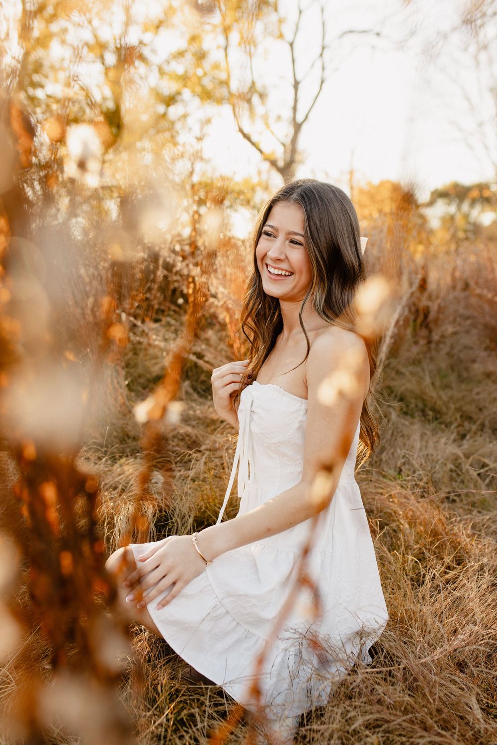 Person in white dress sits gracefully in sunlit autumn field in Frederick Maryland