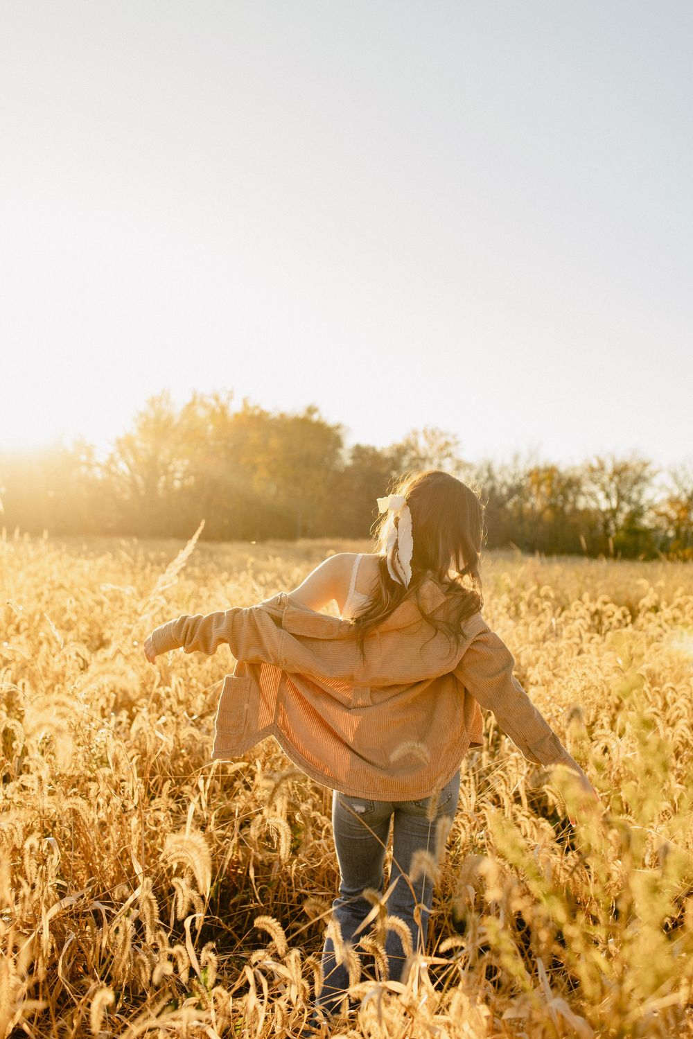 A silhouetted figure twirls in a golden wheat field at sunset.