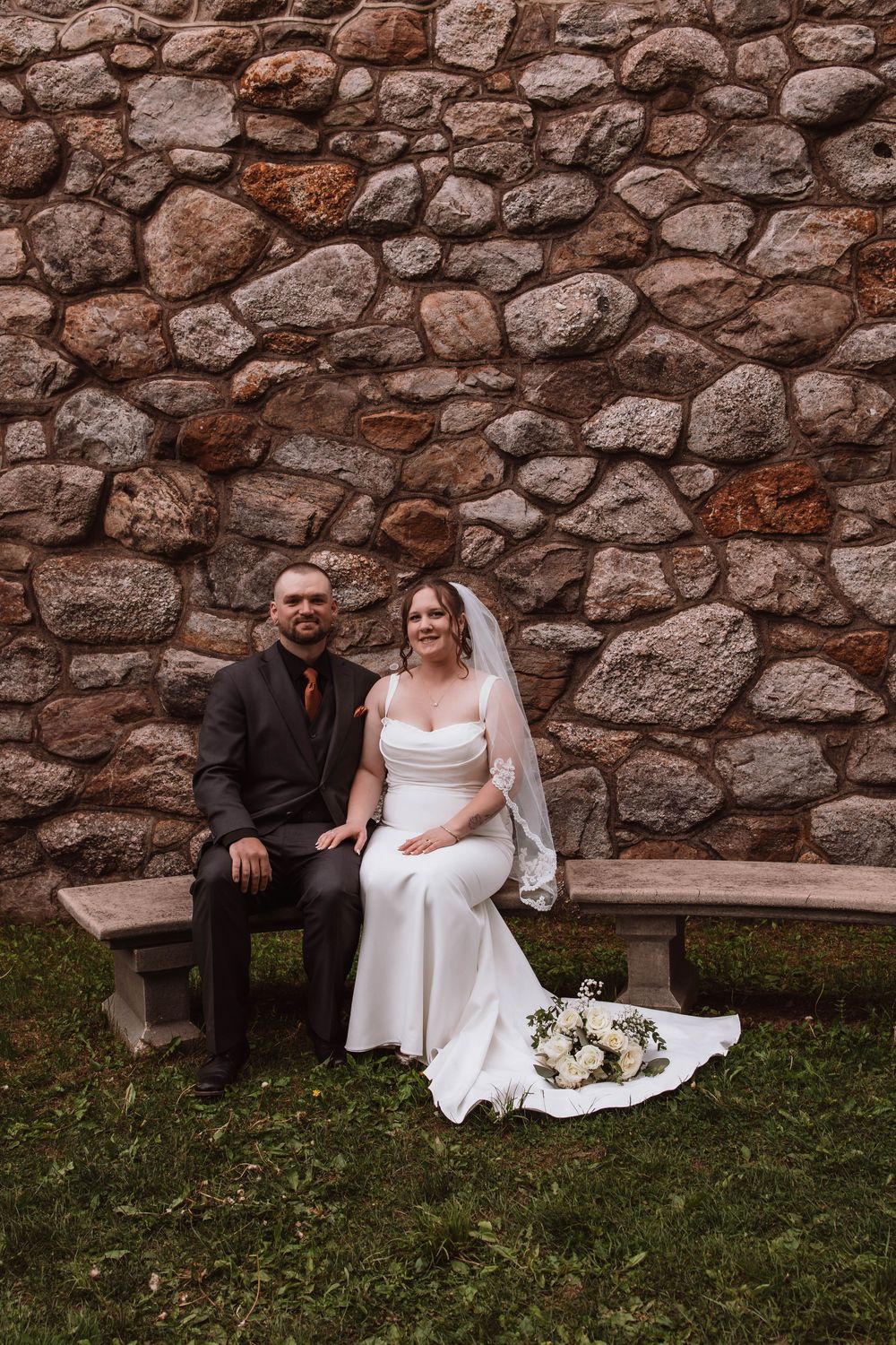 Bride and groom sitting together outside of historic stone church upstate NY