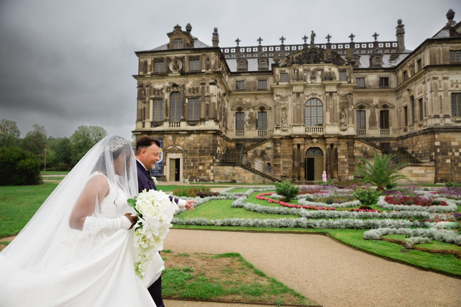 Couple embraces a grand historic palace in Dresden with ornate architecture and manicured gardens. Organized wedding by MyCastleWedding.