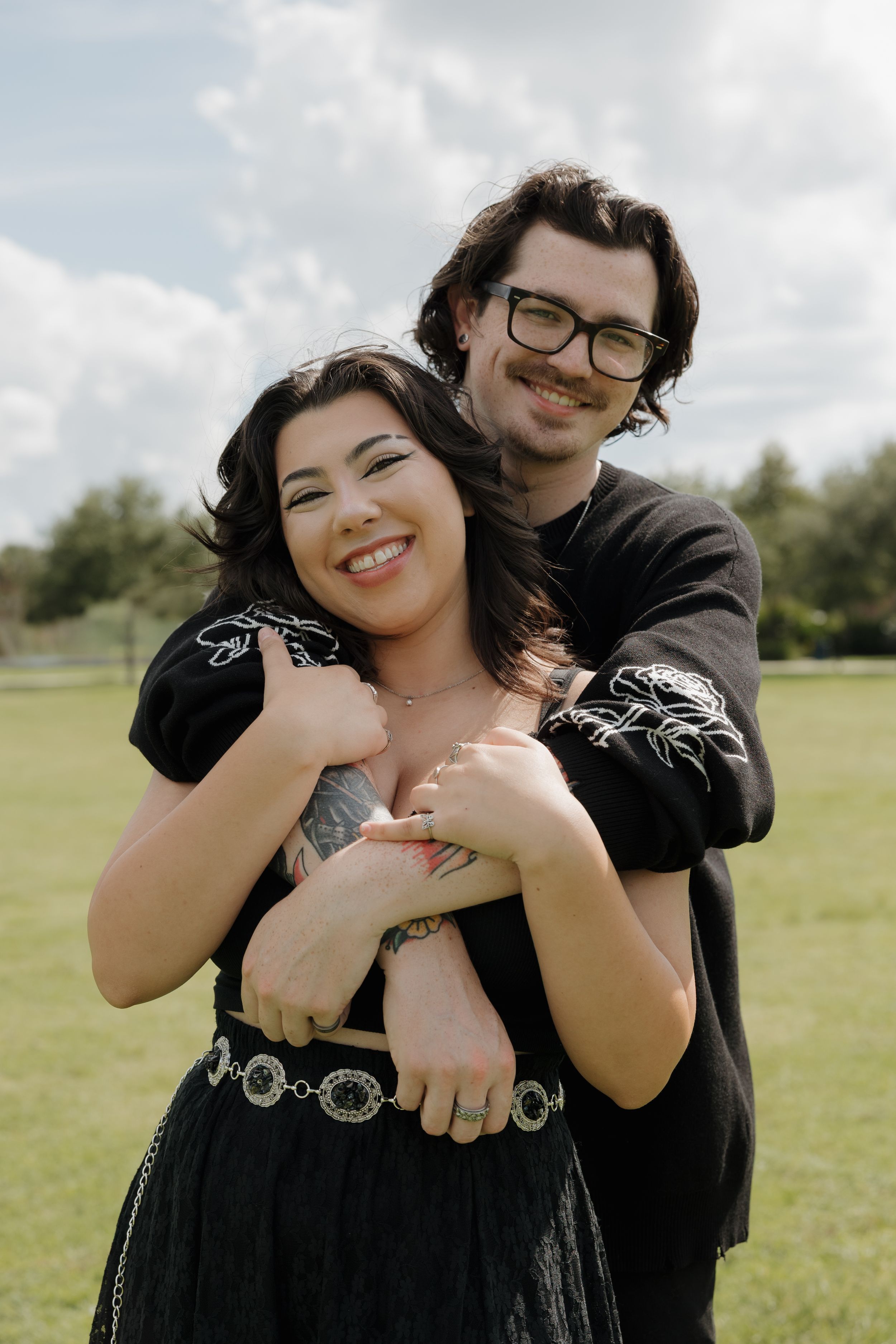 Candid moments of a couple embracing outdoors in a grassy field under cloudy skies.