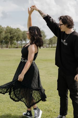 Couple in black outfits dancing and twirling in a sunny green field.
