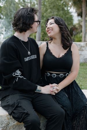Couple in black clothing sharing intimate moments while sitting outdoors.