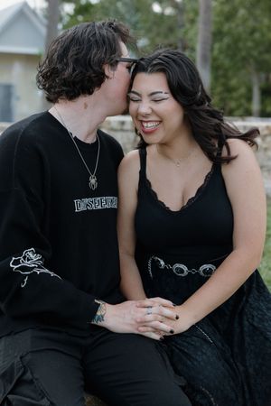 A couple shares tender moments while wearing matching black outfits outdoors.
