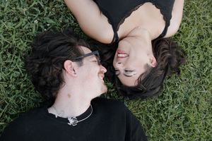Couple lying on grass sharing intimate moments while dressed in black.