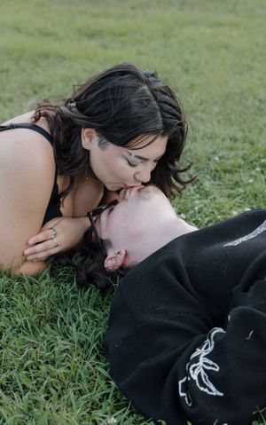 Couple in black clothing shares tender moments while lying in green grass.