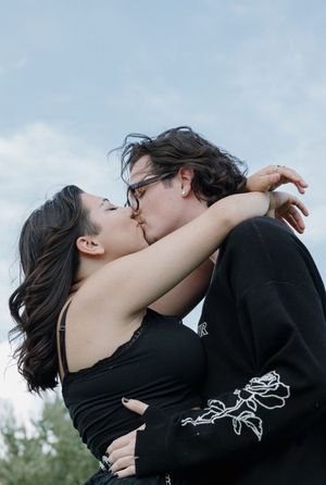 Couple in black clothing embraces against blue sky background.