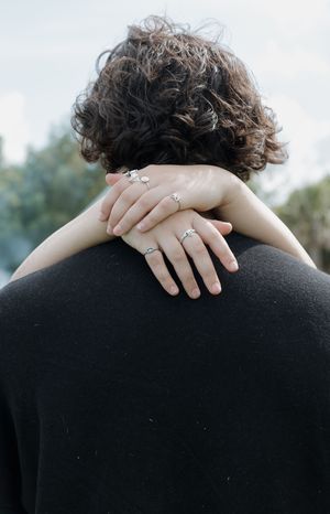 Close-up of hands with rings embracing against a blurred outdoor background.