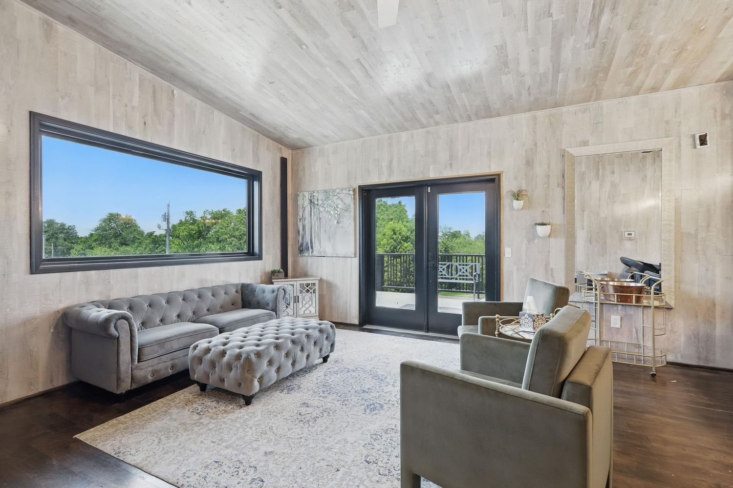 Modern living room with Chesterfield sofa, grey armchair and wood paneled walls featuring large scenic windows.