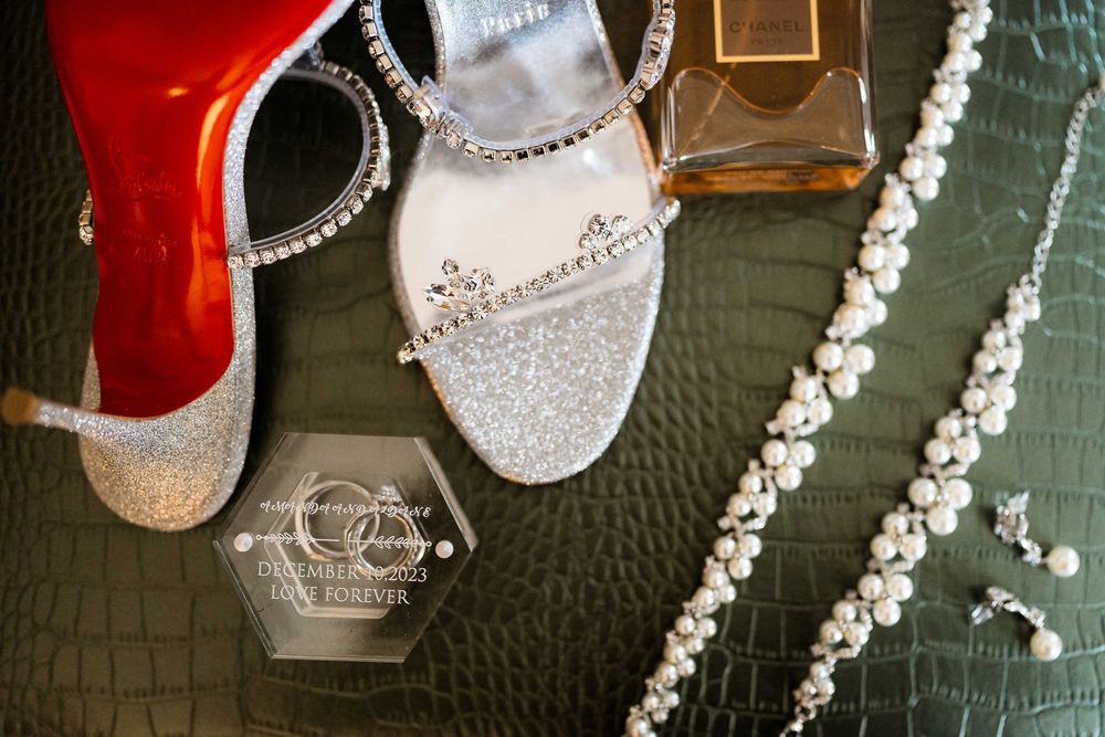 Sparkling bridal accessories including silver glitter heels, pearl necklace and crystal necklace arranged on green leather surface.