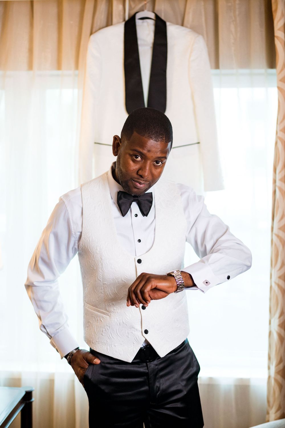 Formal white tuxedo jacket with black lapels hangs on display while someone checks their watch in elegant evening attire.