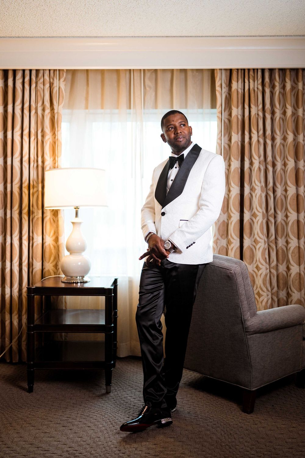 An elegant white dinner jacket with black lapels is worn in a formal hotel room with classic decor.
