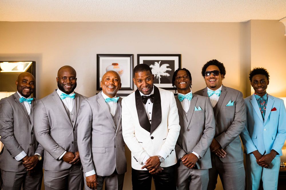 A group of seven people wearing coordinated suits in shades of gray and blue pose together in a formal setting.