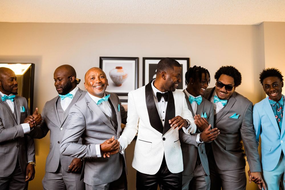 Wedding party wearing coordinating suits in grey, white, and blue tones pose together before the ceremony.