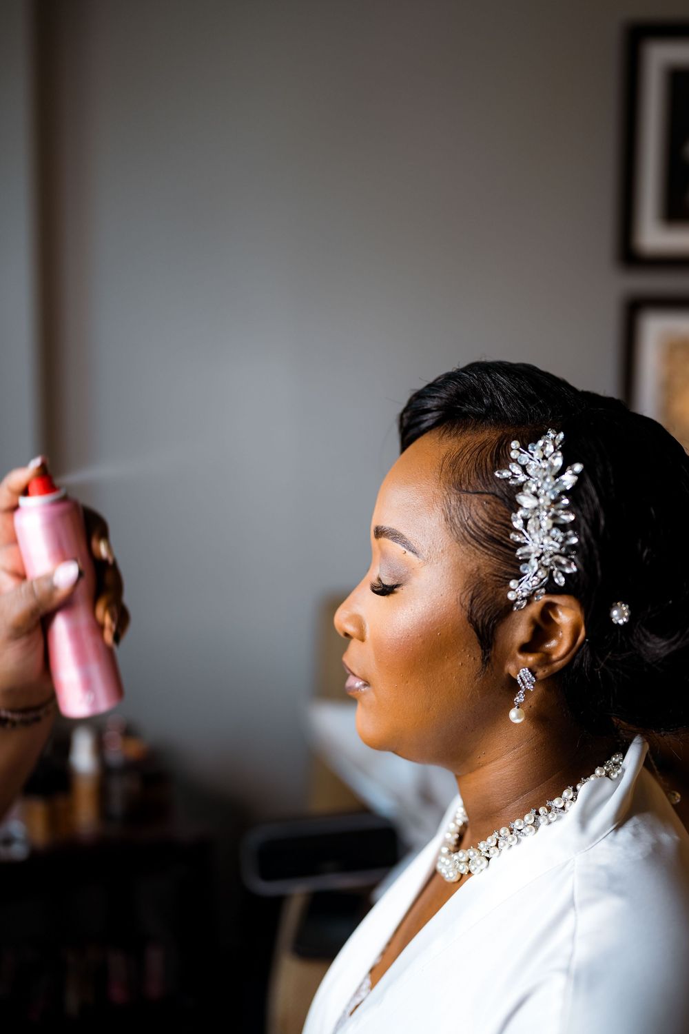 A bride getting her hair styled with a sparkly silver hairpiece and white robe on her wedding day.