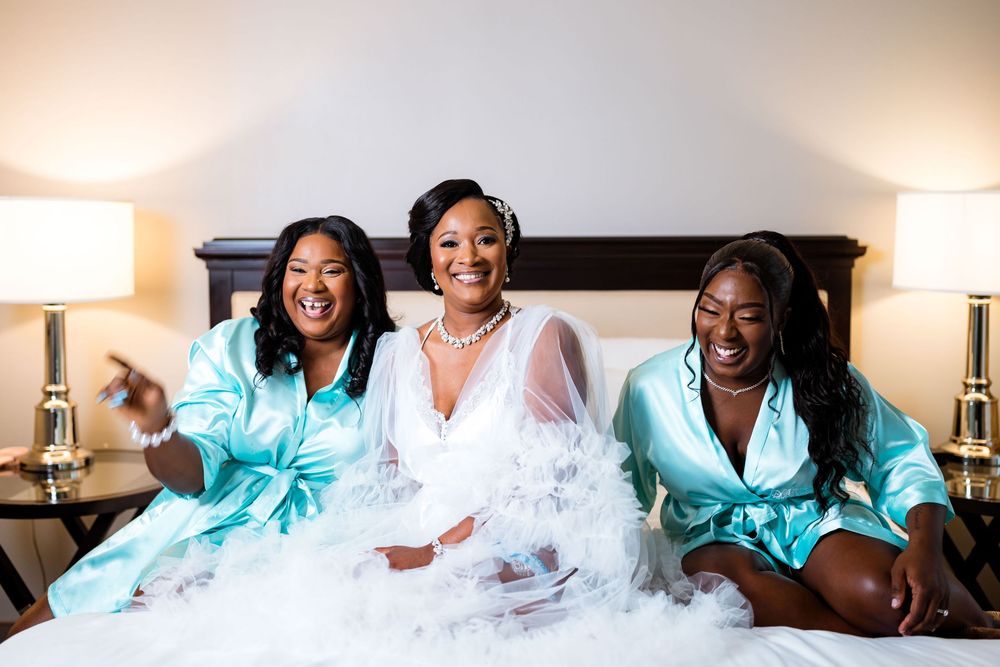Three women in satin robes lounge together on a bed with white tulle fabric during a bridal photoshoot.