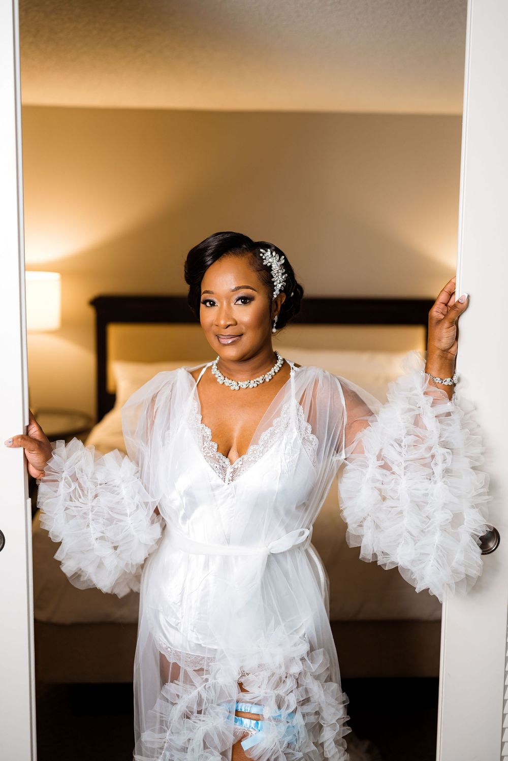 Bride posing in a white lace robe with dramatic bell sleeves and crystal hair accessories.