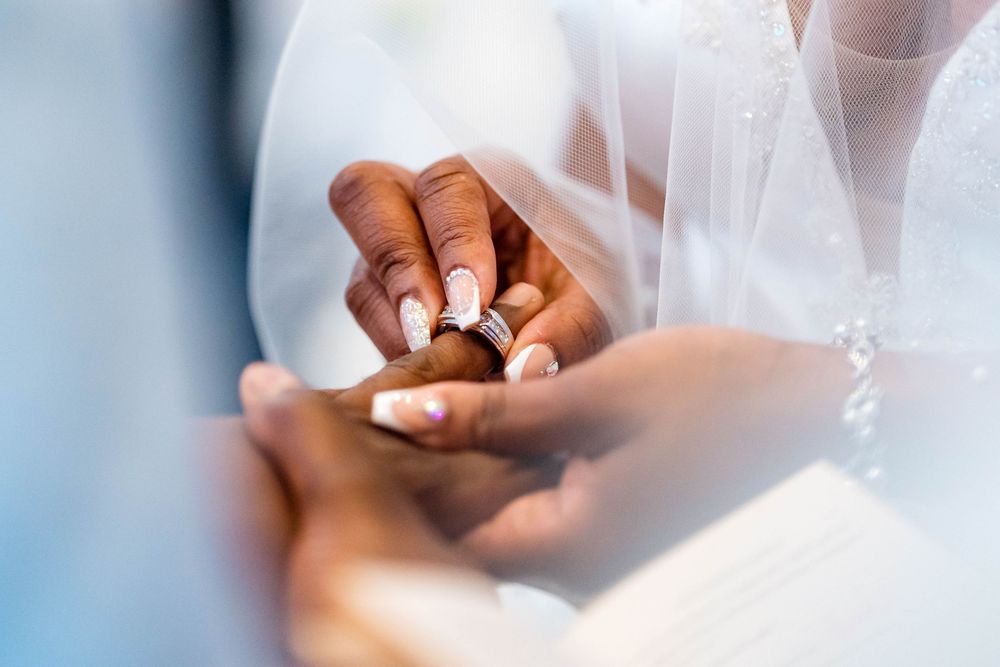 Close up of hands exchanging wedding rings during ceremony with white veil in soft focus.