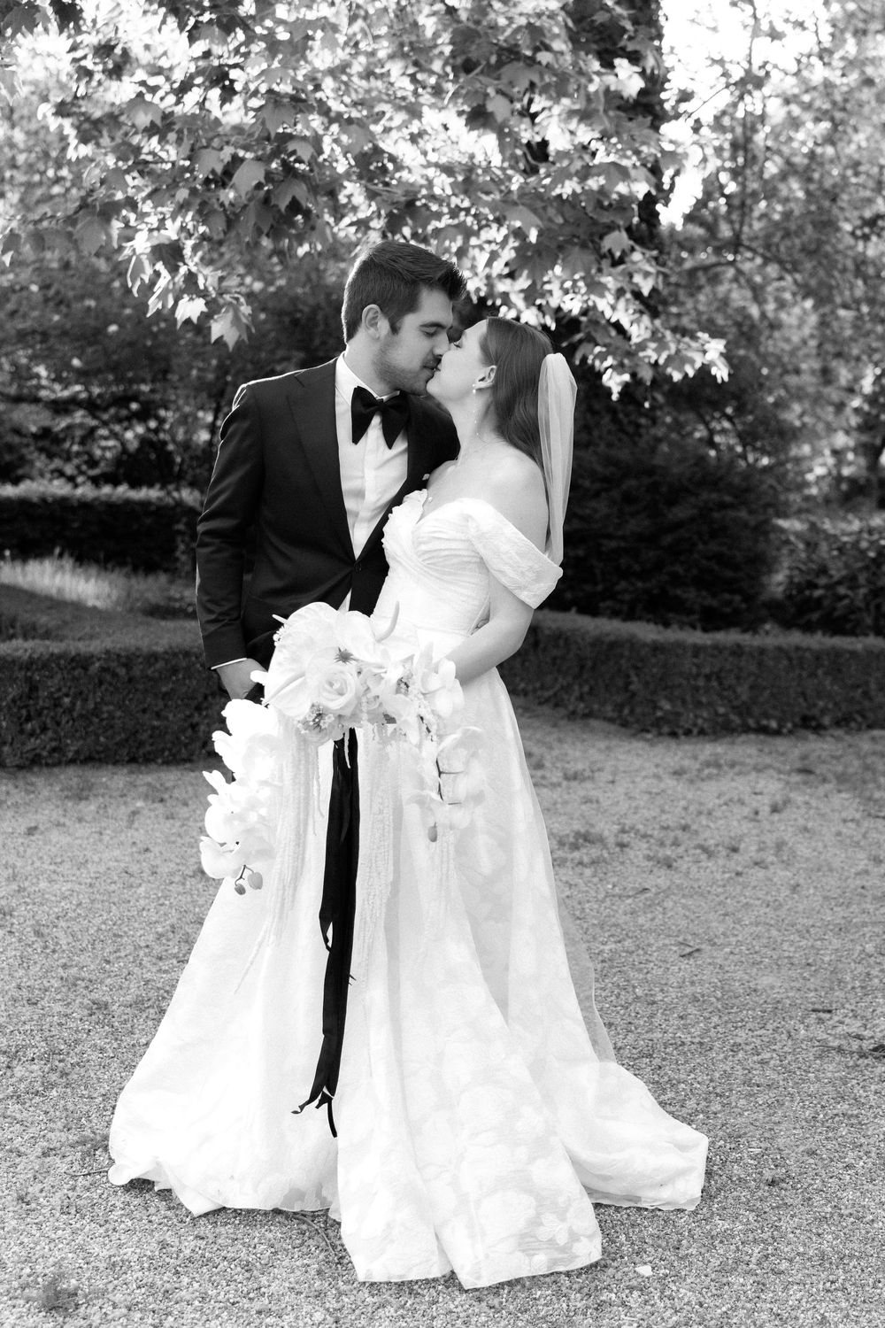 A romantic black and white wedding photo showing a couple embracing outdoors with the bride holding an elegant white bouquet.