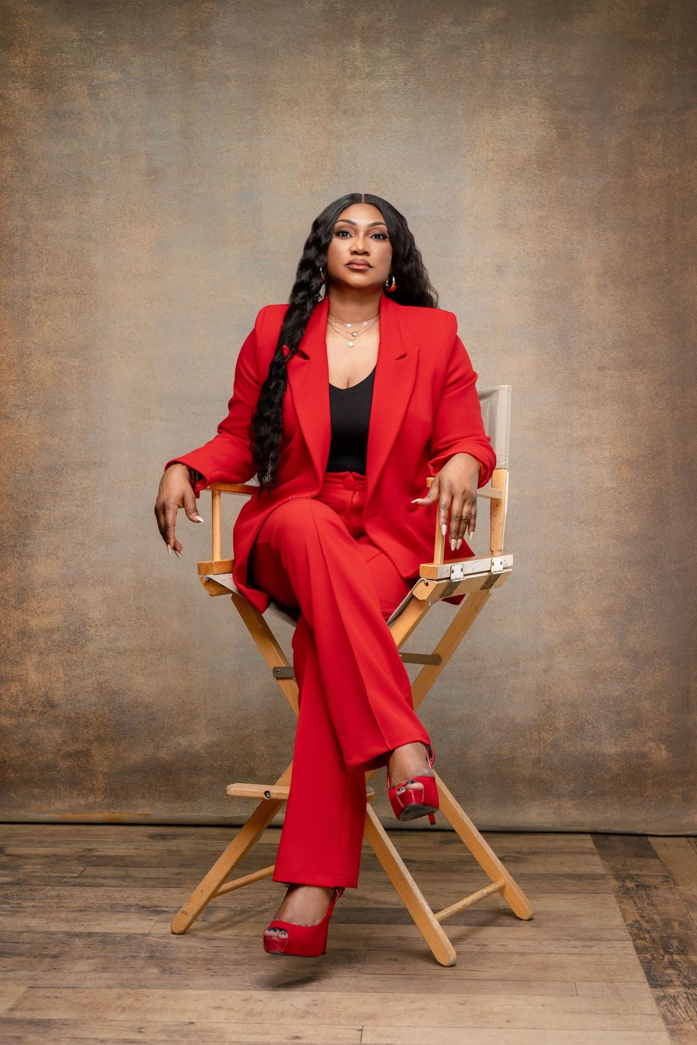 Professional portrait of someone seated confidently in a director's chair wearing a vibrant red power suit and matching heels.