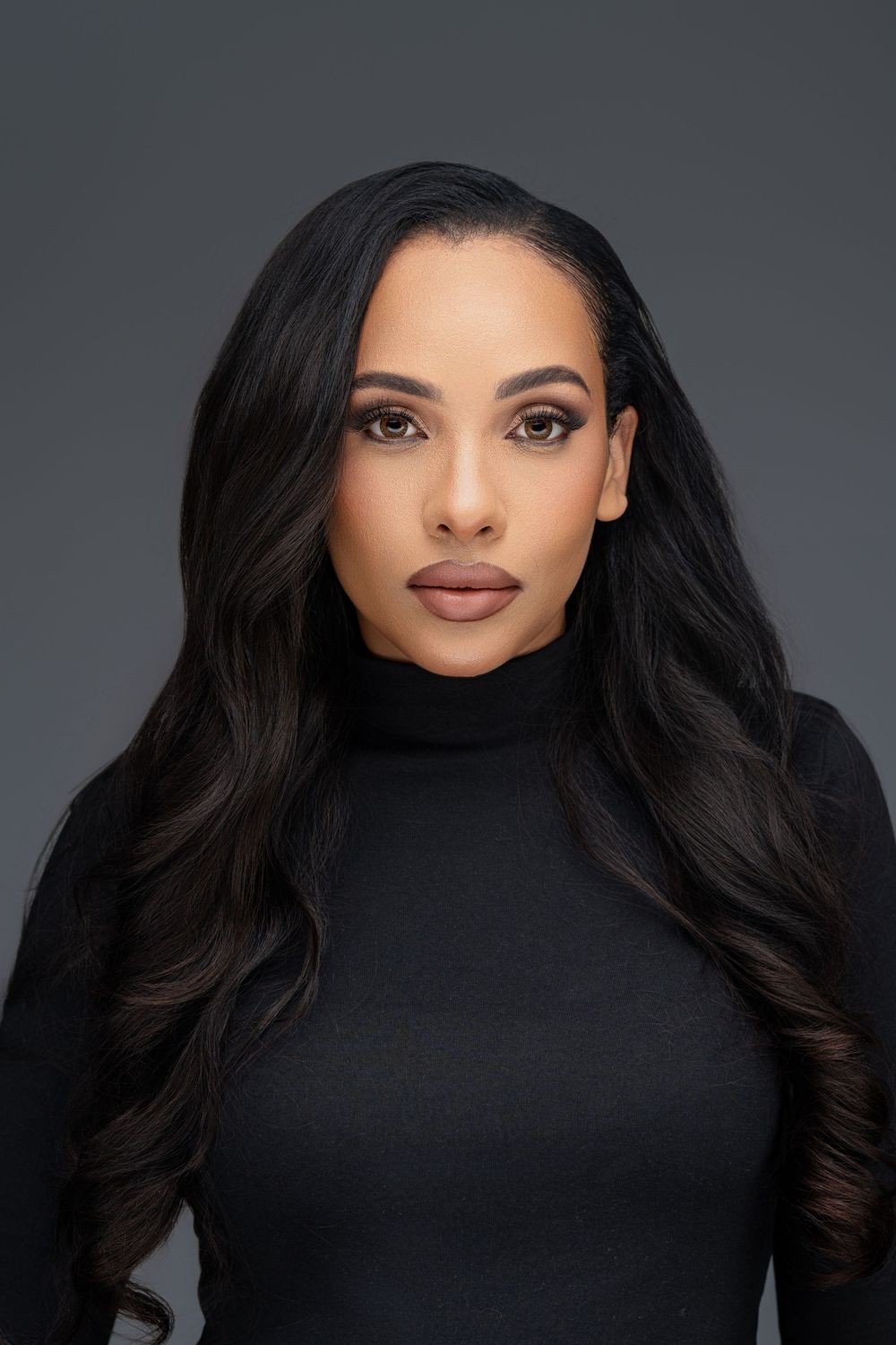Professional studio portrait of a woman with long dark hair wearing a black turtleneck against a gray background.