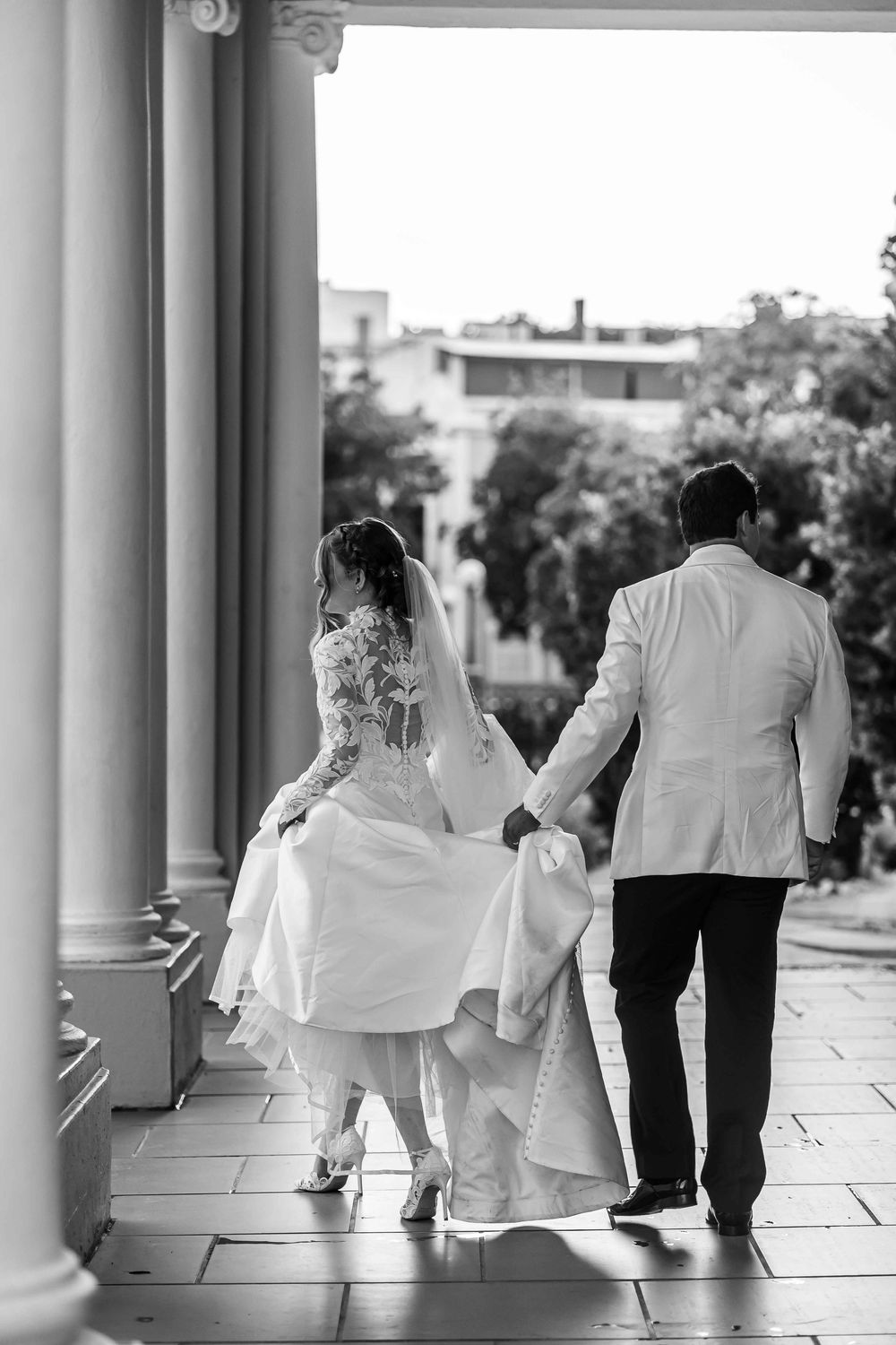 A black and white wedding party walks together across a columned portico in a candid motion shot.