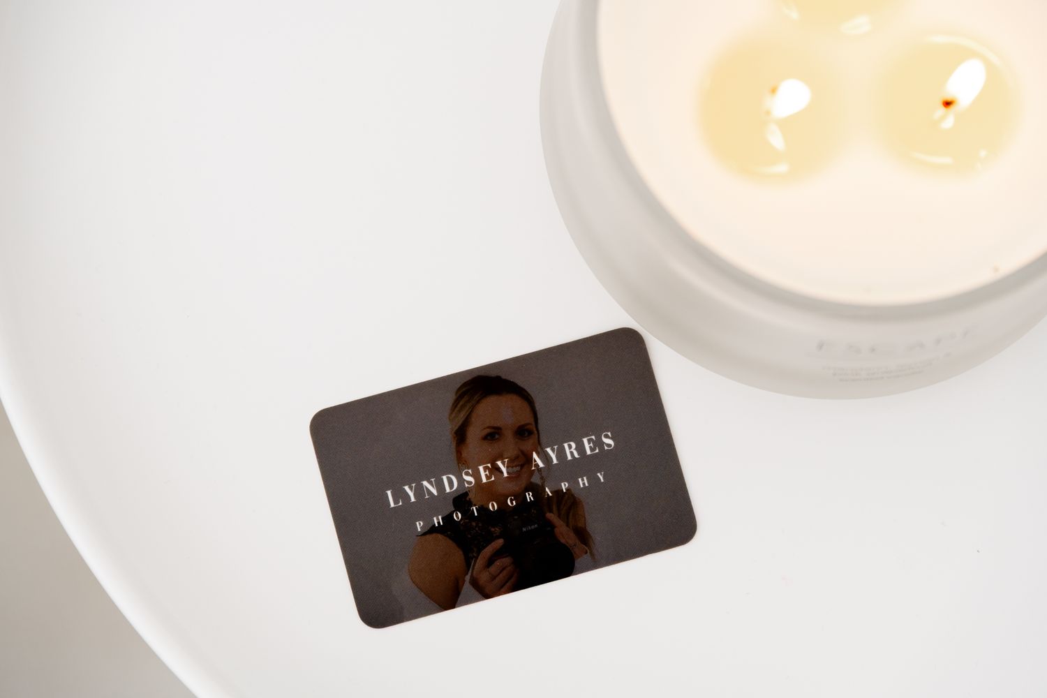 A dark brown store loyalty card sits on a white surface next to a glowing candle.