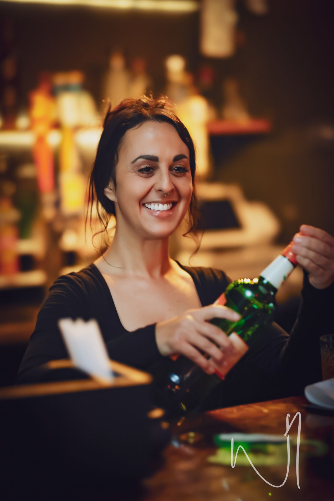 Bartender smiling while serving bottle at dimly lit bar.