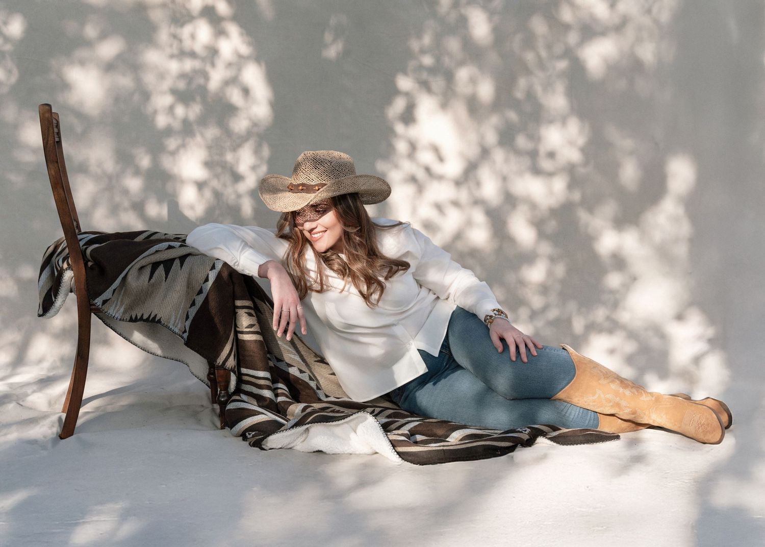 Woman in vintage style clothing reclines elegantly on floor against white backdrop with dramatic lighting and wooden staff.