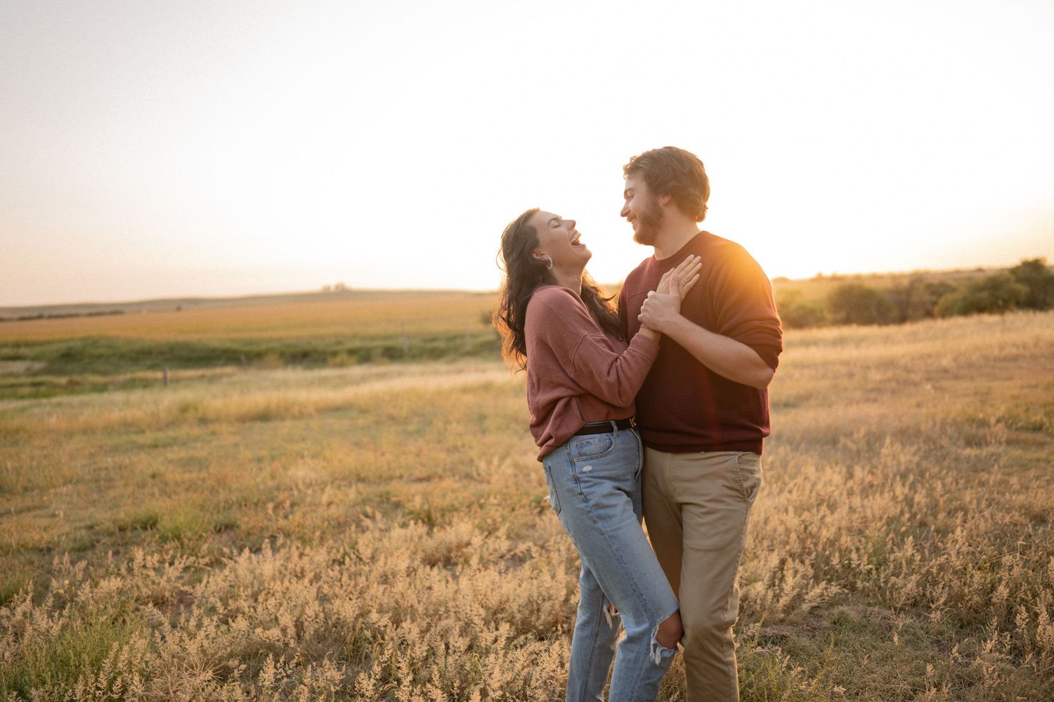 A couple shares a romantic moment at sunset in a golden field during magic hour.