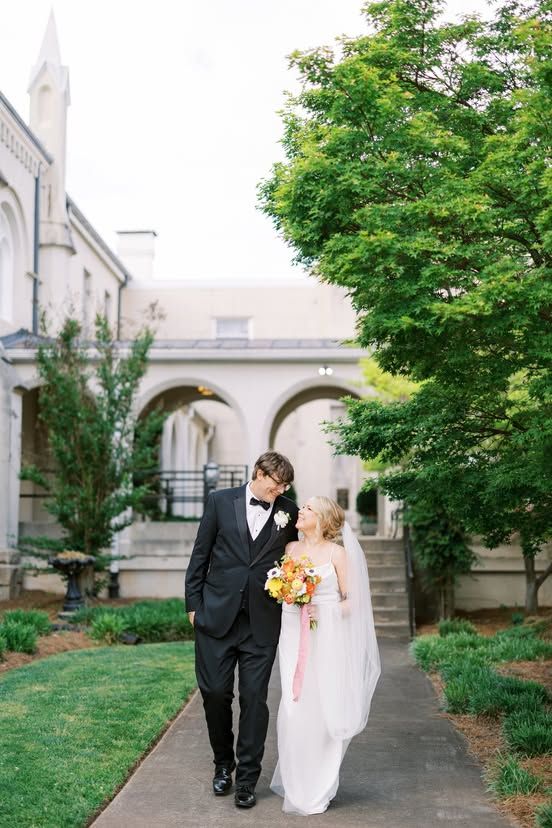 Newlyweds walking along stone pathway beside Gothic-style church architecture.