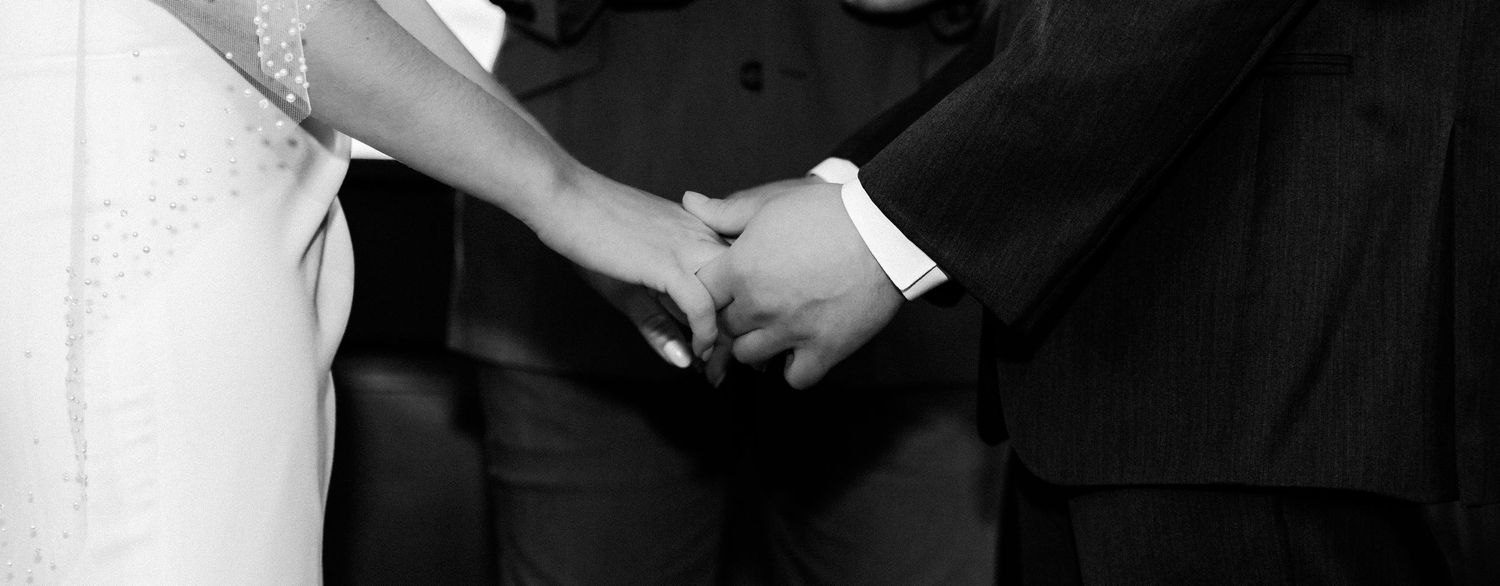 Black and white close-up of bride and groom holding hands during ceremony.