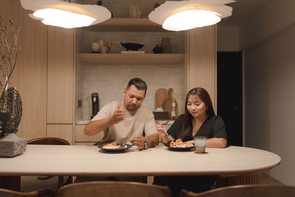 Two people enjoy a meal together at a dining table under modern pendant lights in a cozy home setting.