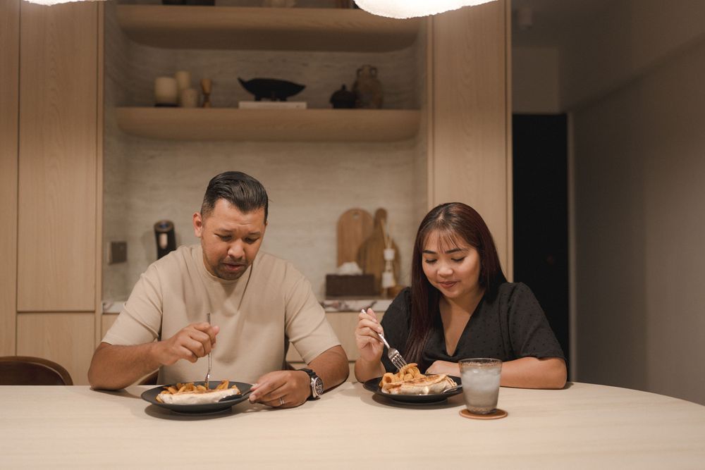 Two people share a meal together at a minimalist white dining table in a cozy home setting.