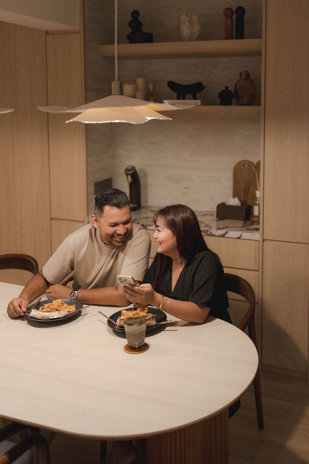 Two people sharing a cozy meal at a round white table under warm lighting in a modern dining space.