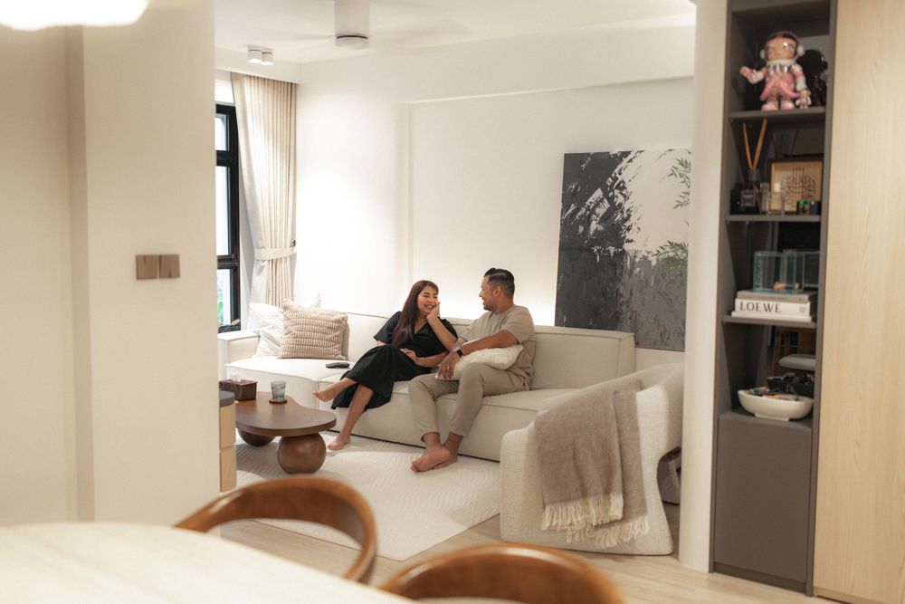 A cozy modern living room features a white sectional sofa, with decorative shelving and natural light streaming through a window.