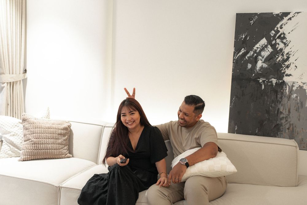 A couple sits together on a white couch in a minimalist living room with black and white artwork on the wall.