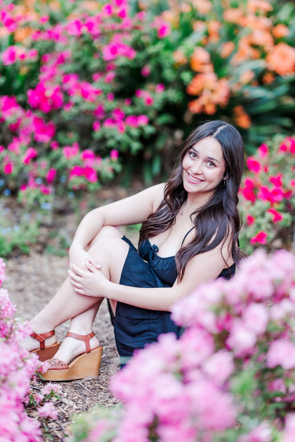 A portrait taken in a garden with vibrant pink and orange flowers in full bloom.