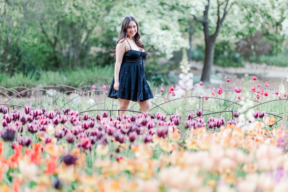 A woman in a navy dress stands among colorful tulips blooming in a spring garden.